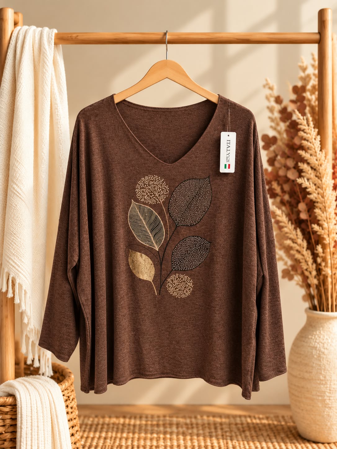 Vue de face sur cintre du pull Feuilles framboise à col V et manches longues, avec motif végétal central composé de feuilles dorées et foncées et de formes rondes pointillées.