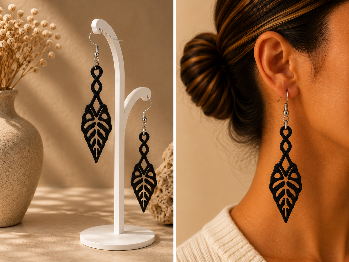 Boucles d’oreilles longues noires au motif de feuille d’alocasia ajourée, présentées sur support et portées