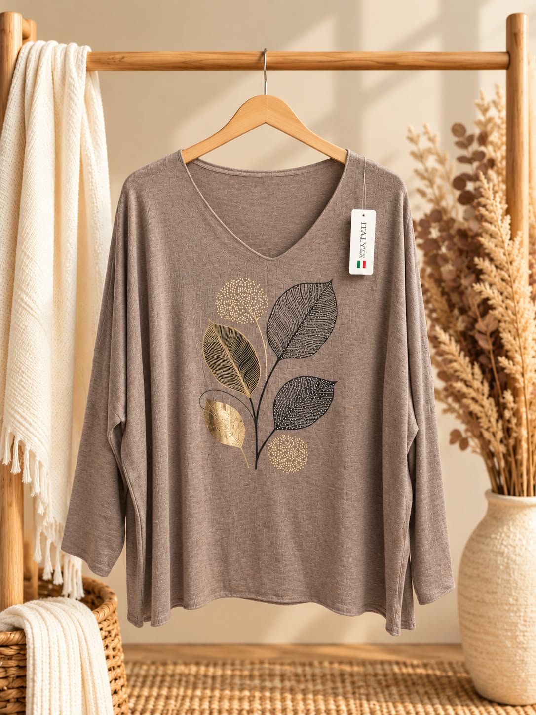 Vue de face sur cintre du pull Feuilles taupe à col V et manches longues, avec motif végétal central composé de feuilles dorées et foncées et de formes rondes pointillées.